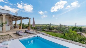 A swimming pool with lounge chairs and a pergola, surrounded by a stone wall and greenery, with a view of the countryside. - Hilly Trullo with Sea View (Leuca)