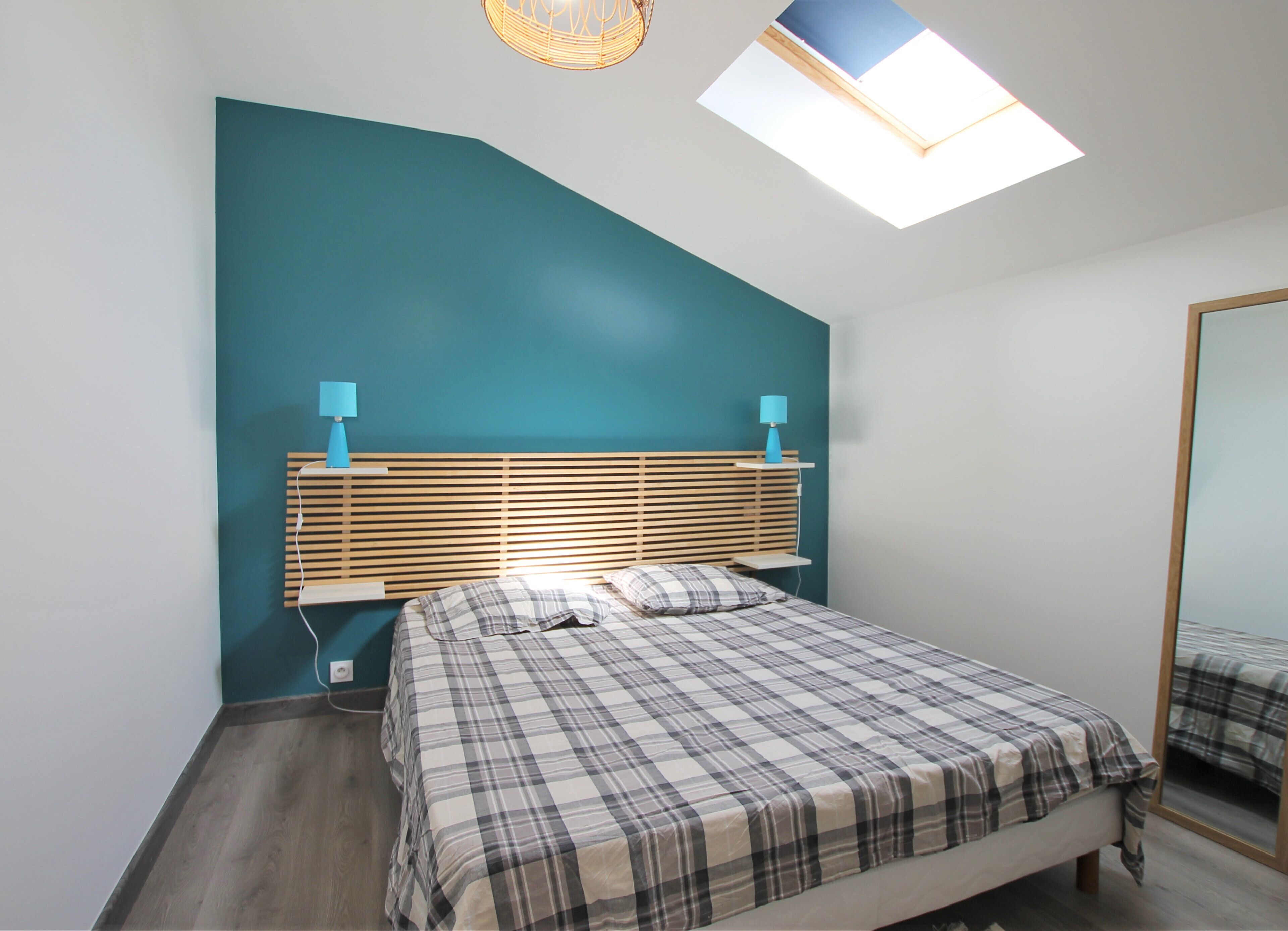 A bedroom with a sloped ceiling, a skylight, a bed with a plaid bedspread, and two bedside lamps.