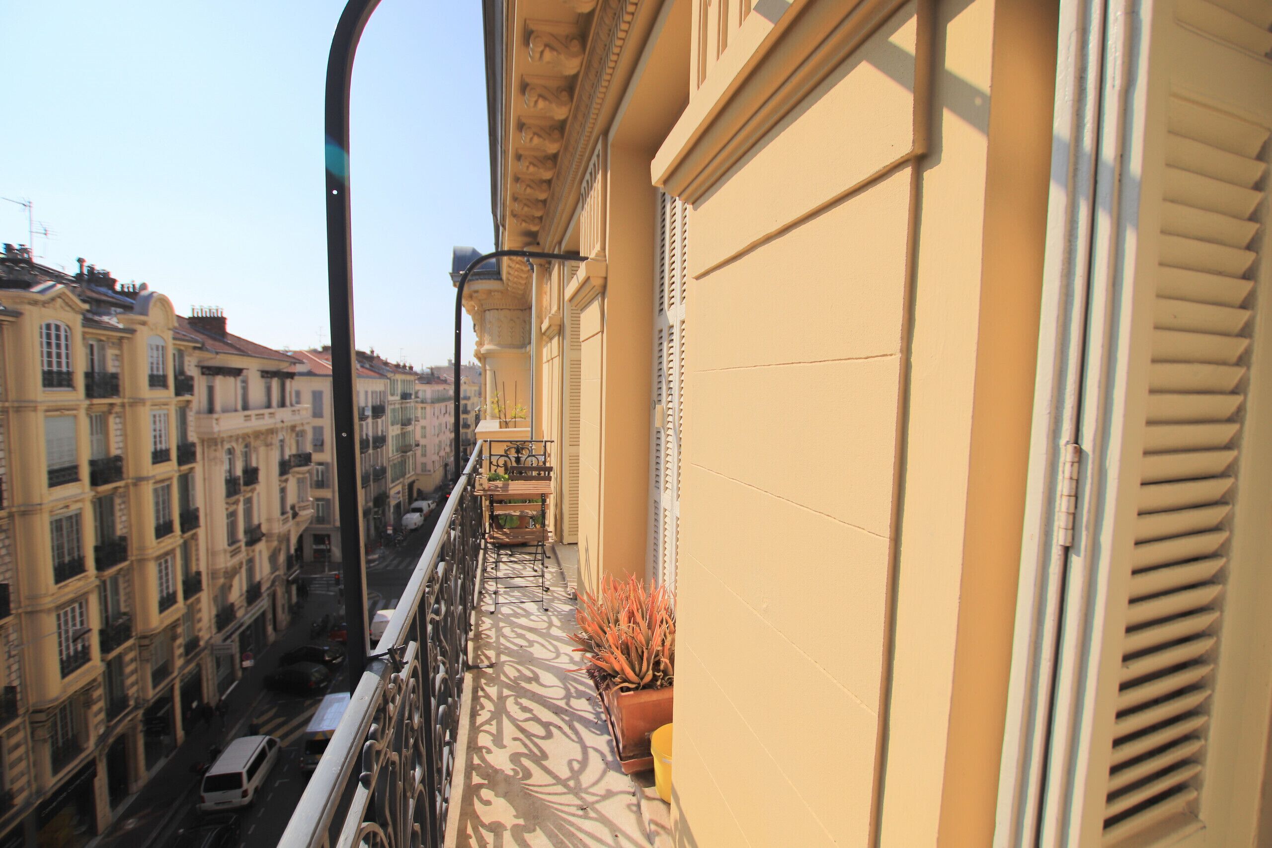 A balcony with a view of a city street, a potted plant, and a building with classical architecture.