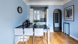 Een moderne keuken met een eethoek, met een zwart aanrecht, witte stoelen en een klok aan de muur.