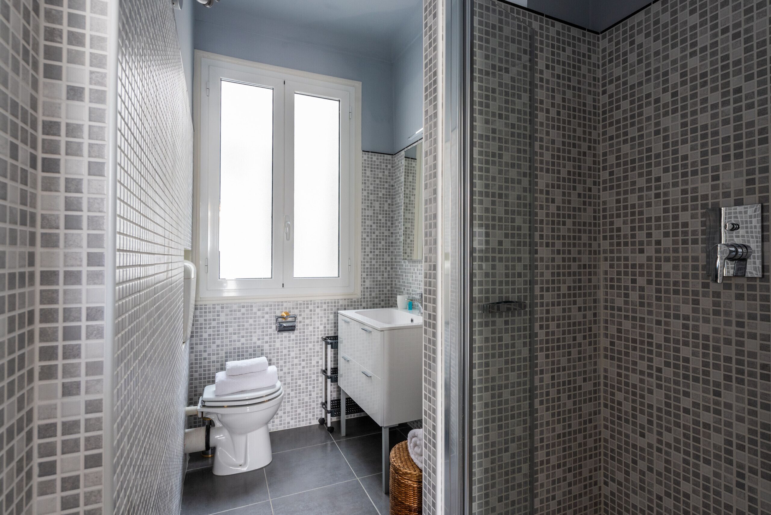 Een badkamer met toilet, wastafel en douche, met betegelde wanden en een raam.