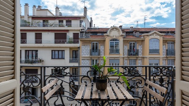 Een balkon met een houten tafel en een bloempot, met uitzicht op een rij gebouwen met balkons en ramen.