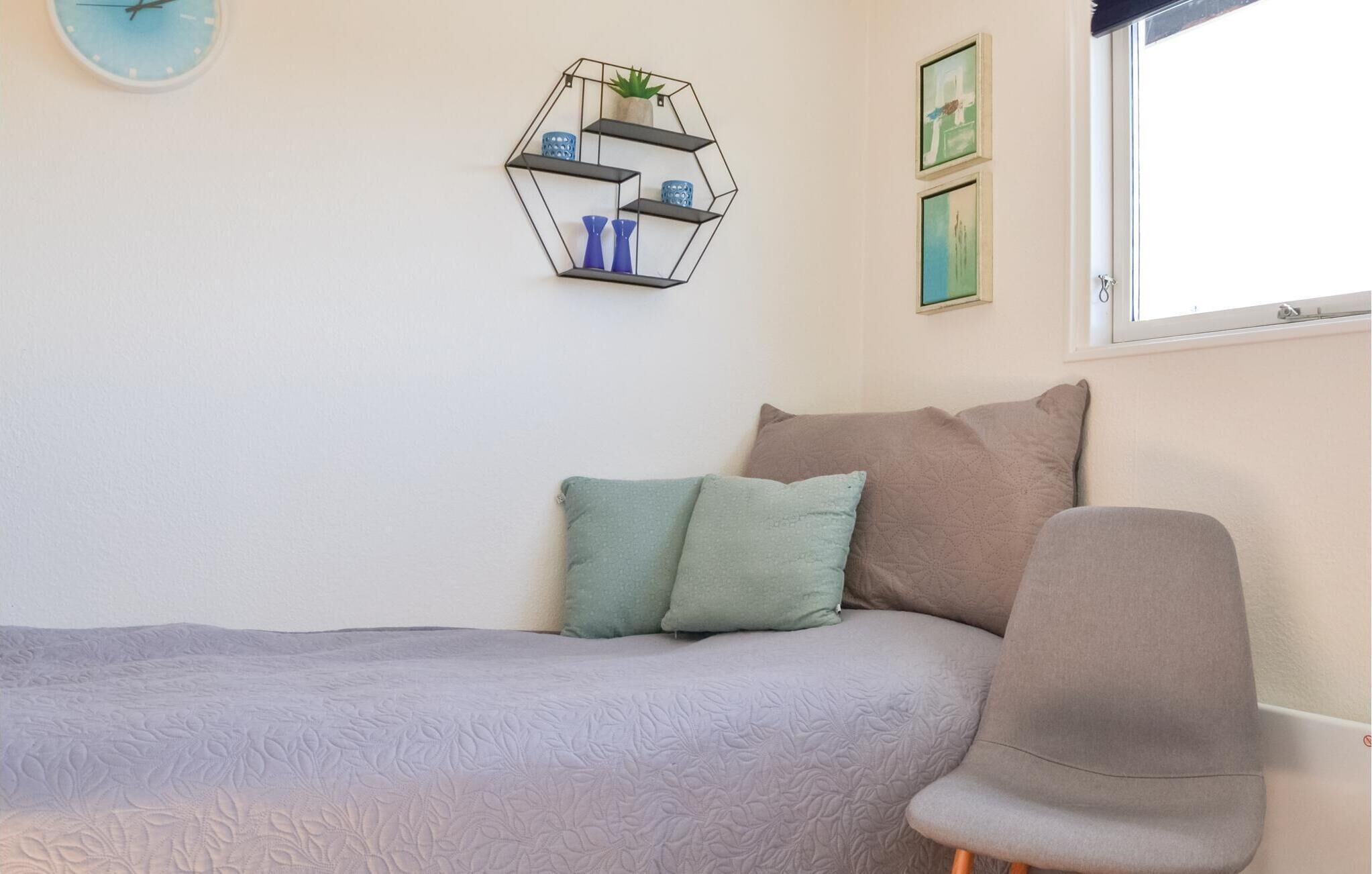 A bedroom with a bed, pillows, a chair, a wall clock, a hexagonal shelf with decorative items, and framed pictures.