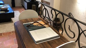 A dining area with a wooden table, chairs, and a book. There is a TV and a painting on the wall.