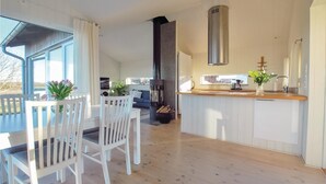Eine moderne Küche mit einer zentralen Kochinsel, einem Essbereich mit weißen Stühlen und einem großen Fenster für natürliches Licht.