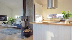 Eine moderne Küche mit einer zentralen Kochinsel, einem eingebauten Holzofen und einem großen Fenster für natürliches Licht.