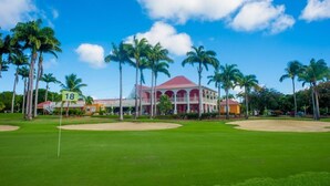 Un terrain de golf avec un bâtiment en arrière-plan, des palmiers et un ciel bleu dégagé.