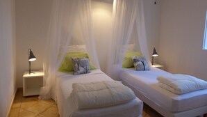 Une chambre avec deux lits, chacun doté d’un baldaquin, de draps blancs et d’oreillers verts. Il y a des tables de chevet avec des lampes.