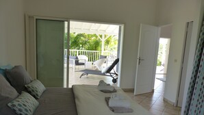 Une chambre à coucher avec un lit, des oreillers, une serviette et une vue sur un balcon extérieur équipé de chaises et d’une table.