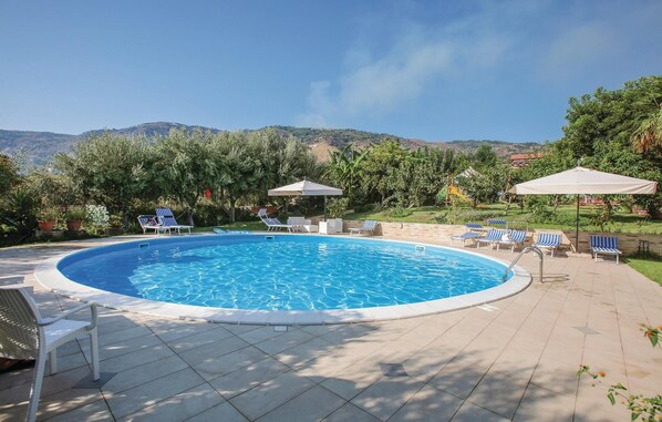 A circular swimming pool with lounge chairs and umbrellas, surrounded by a landscaped garden and hills in the background. - Cozy home in Joppolo with WiFi (Joppolo)