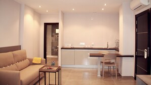 A modern living room with a sofa, a small table, and a kitchen area with a dining table and chairs.