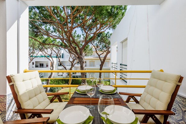 Una mesa de comedor con cuatro sillas, vista a un árbol y edificios al fondo.