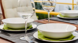 Une table à manger dressée avec des assiettes, des verres et des couverts, donnant sur un paysage verdoyant et un bâtiment en arrière-plan.