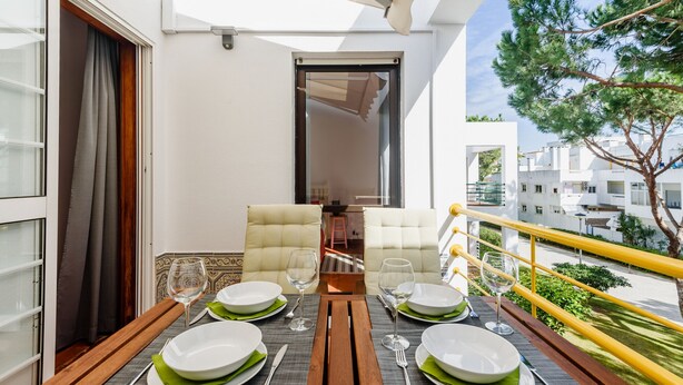 Un balcon aménagé avec un coin repas, comprenant une table, des chaises et une vue sur les bâtiments et la végétation environnants.