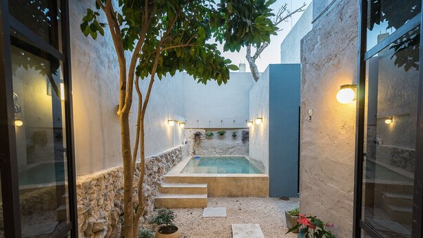 A private outdoor pool area with stone steps leading to a hot tub, surrounded by walls and potted plants.