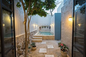 Uma área de piscina privativa ao ar livre, com escadas de pedra que levam a uma banheira de hidromassagem, cercada por paredes e plantas em vasos.