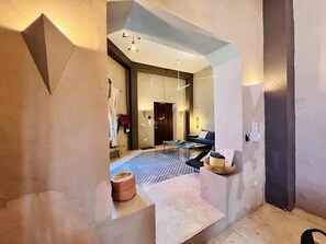 Un interior moderno con una zona de estar central, una mesa de comedor y una puerta visible que conduce a otra habitación.