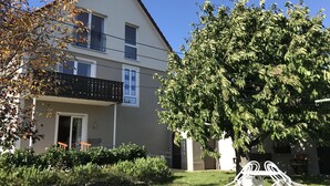 Ein zweistöckiges Gebäude mit Balkon, umgeben von Grünpflanzen und einem Baum.