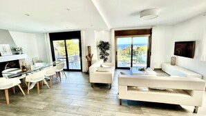 A modern living room with a glass dining table, white sofas, and a view of the outdoors.