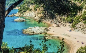 A coastal beach with clear waters, rocky outcrops, and a sandy shore.