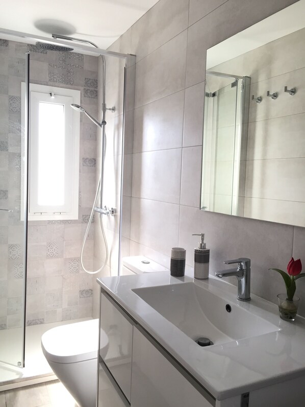 A modern bathroom with a glass-enclosed shower, a white sink, and a large mirror.