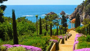 A garden with a pathway leading to a gazebo overlooking the sea.