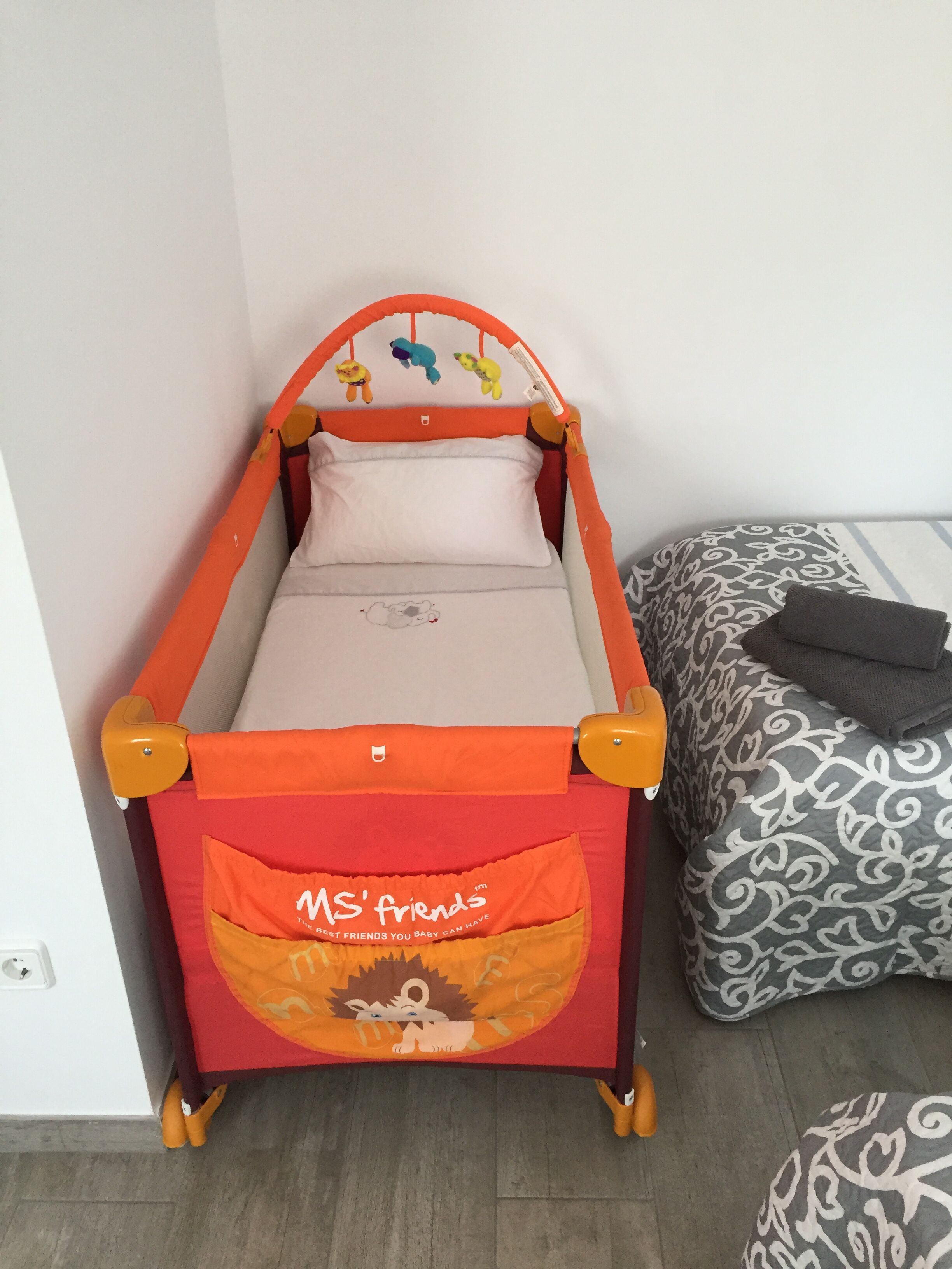 Ein Kinderbett mit Löwenmotiv, ein Kissen mit Muster und ein kleiner Nachttisch.