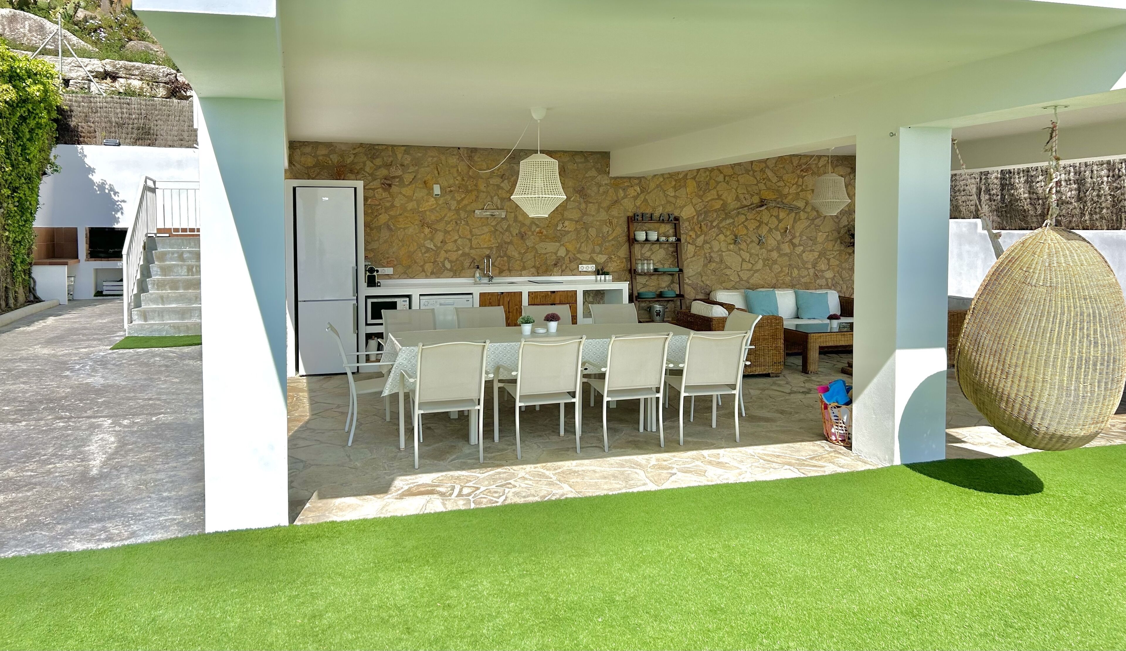 Eine moderne Küche mit Steinrückwand, ein Essbereich mit weißen Stühlen und eine Sitzecke mit einer Couch und Kissen.