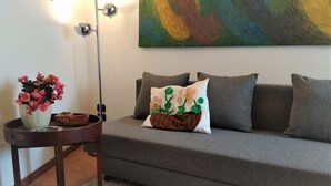A grey sofa with a floral pillow and a small table with a vase of pink flowers.