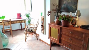 A room with a wooden desk, wicker chairs, a cabinet with drawers, and potted plants.