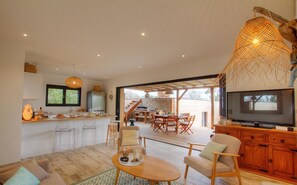 A modern kitchen with a dining area, a TV, and a wooden dining table. - LES PIEDS DANS L'EAU Jacuzzi and beach for 2 to 8 people (Coti-Chiavari)