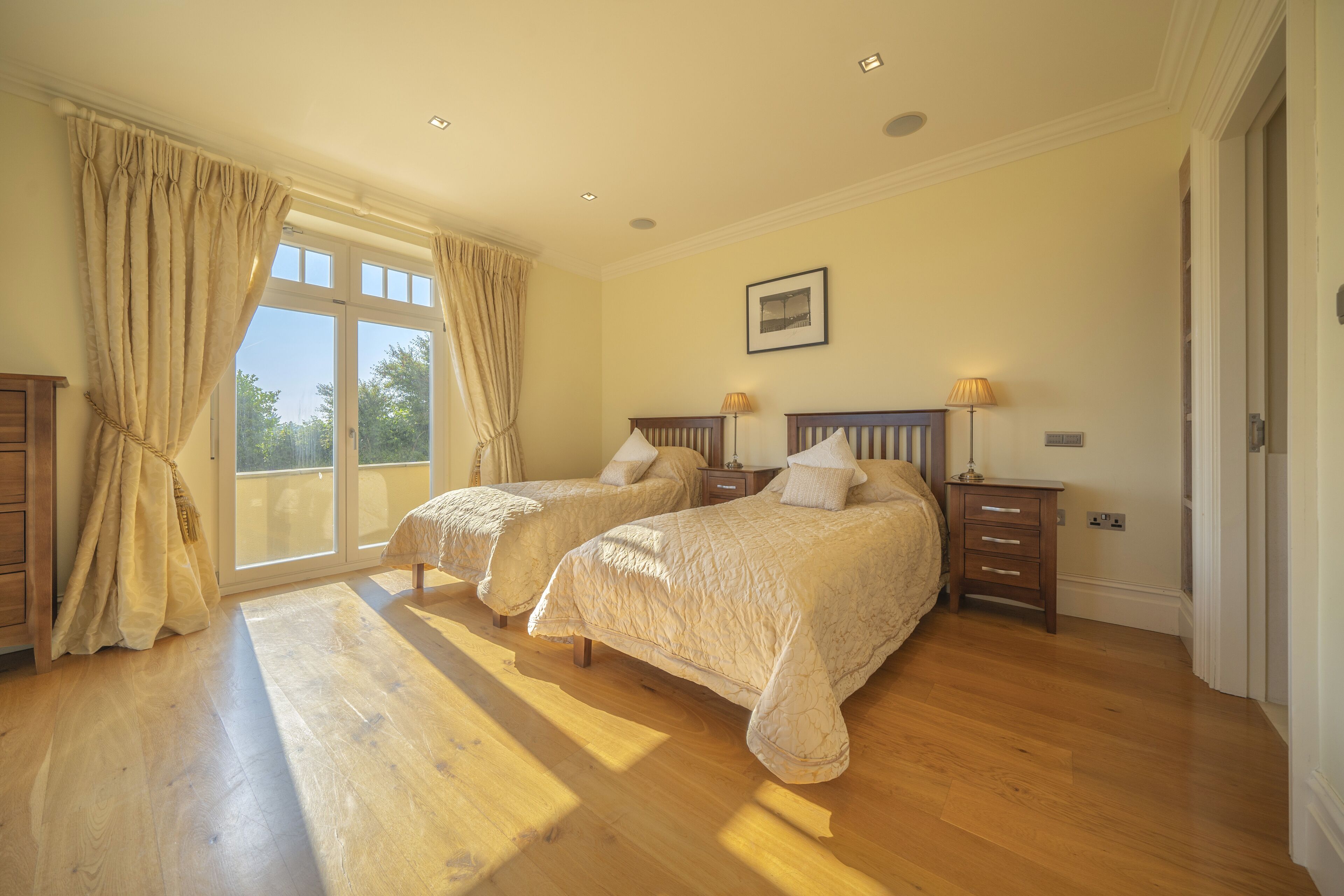 A bedroom with two beds, a large window with curtains, and a wooden floor.