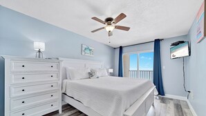 A bedroom with a bed, a dresser, a ceiling fan, a TV, and a window with curtains.
