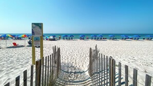 A beach with a wooden fence leading to the water, blue umbrellas, and beach chairs.