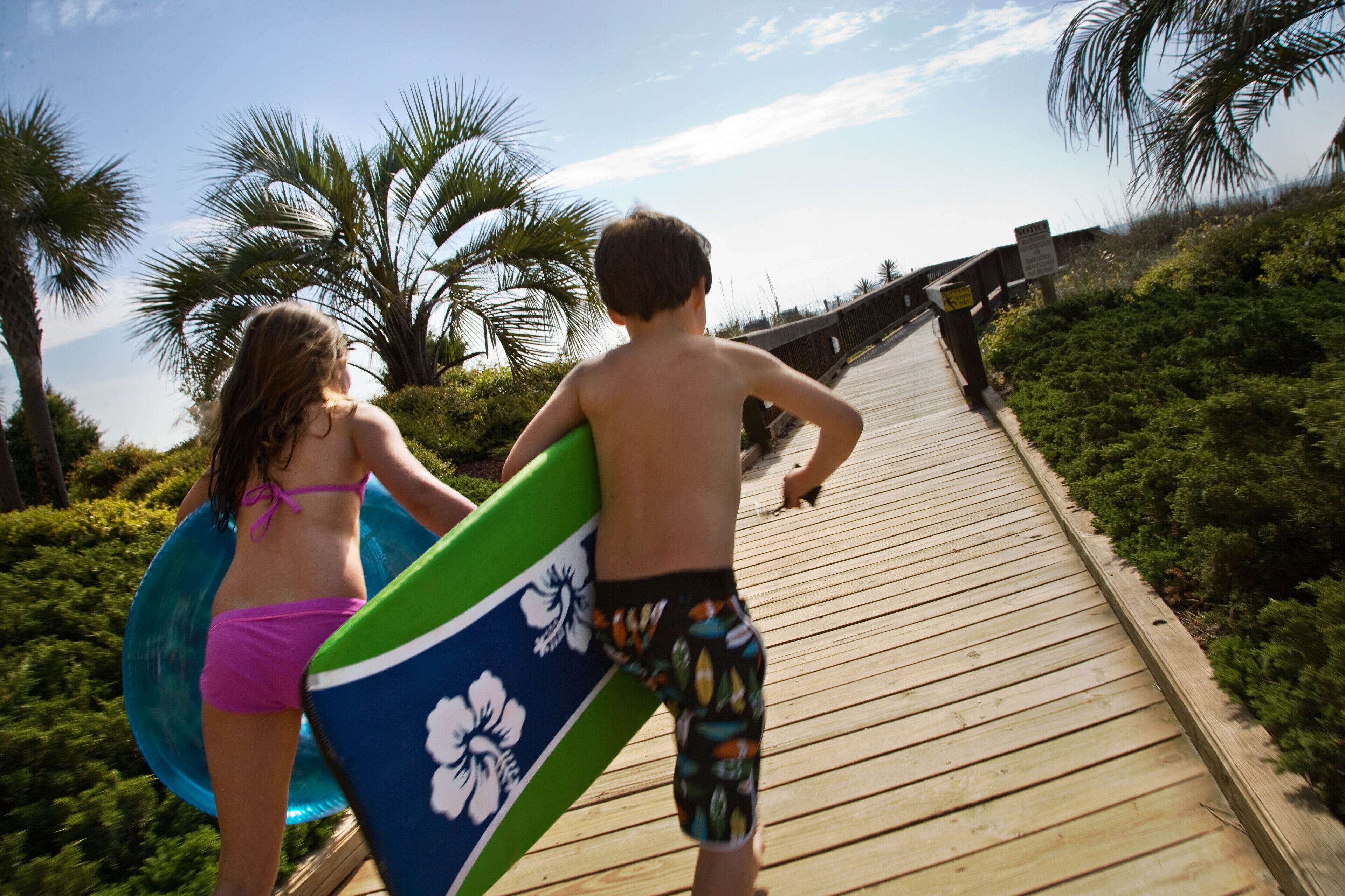 A wooden boardwalk with palm trees and a clear sky.