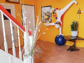 Un couloir avec une rambarde blanche, une plante en pot, une sculpture et un tableau encadré au mur.