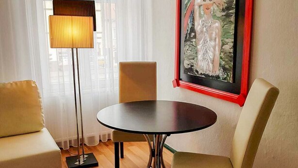 Una habitación con una mesa redonda, dos sillas, una lámpara de pie y un cuadro en la pared.