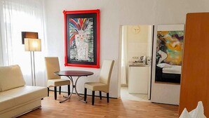 Habitación de hotel con cama, sofá, mesa de comedor y dos sillas. Hay un cuadro en la pared y un reloj también.