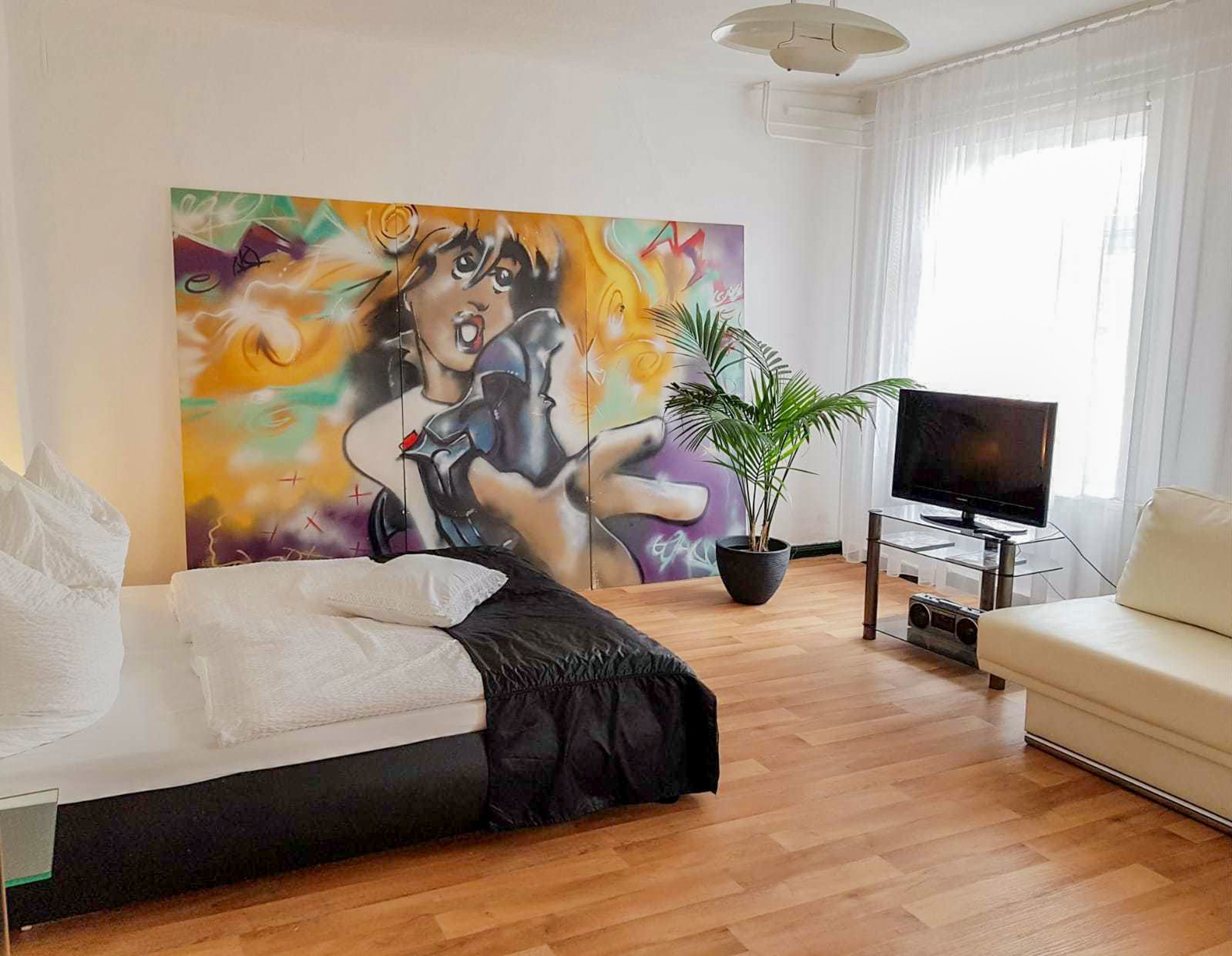 Ein modernes Schlafzimmer mit einem Bett, einem Fernseher und einem großen, abstrakten Gemälde an der Wand.