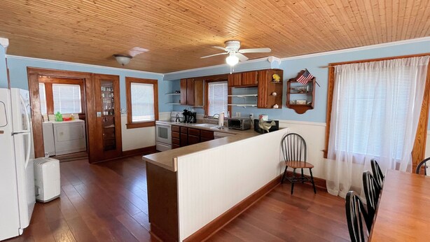 A spacious kitchen with wooden cabinets, a central island, and a dining area with a table and chairs. - Blue Water - Single Family Home - In Town - LG. FENCEED IN YARD, NO LINENS (Chincoteague)