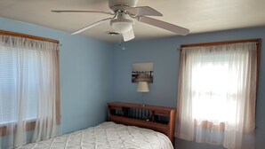 A bedroom with a bed, a ceiling fan, a nightstand, and a window with sheer curtains. - Blue Water - Single Family Home - In Town - LG. FENCEED IN YARD, NO LINENS (Chincoteague)