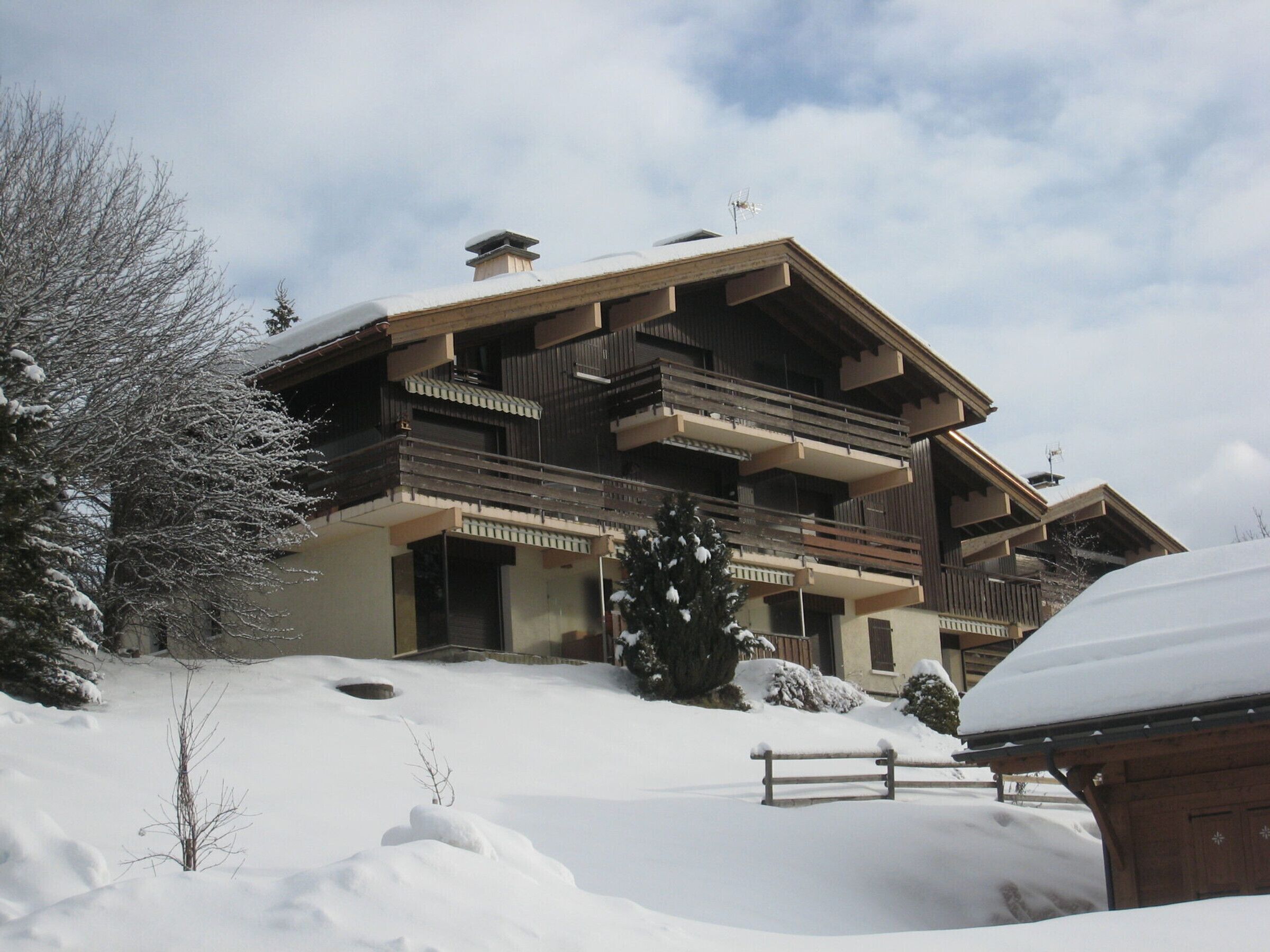 A multi-story building with balconies, surrounded by snow-covered ground and trees.