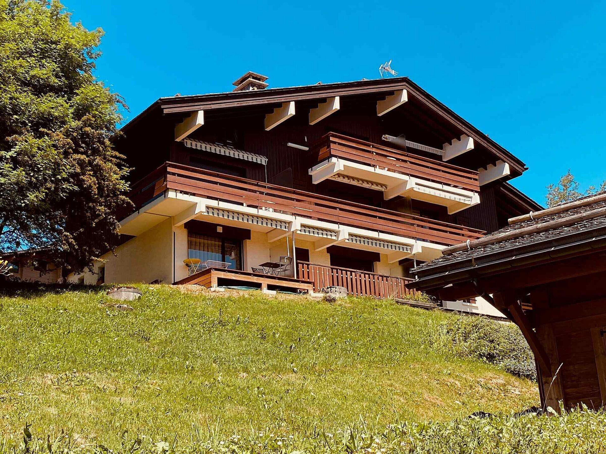 Un chalet à plusieurs étages doté de balcons, d’une façade en bois et situé sur une colline verdoyante.