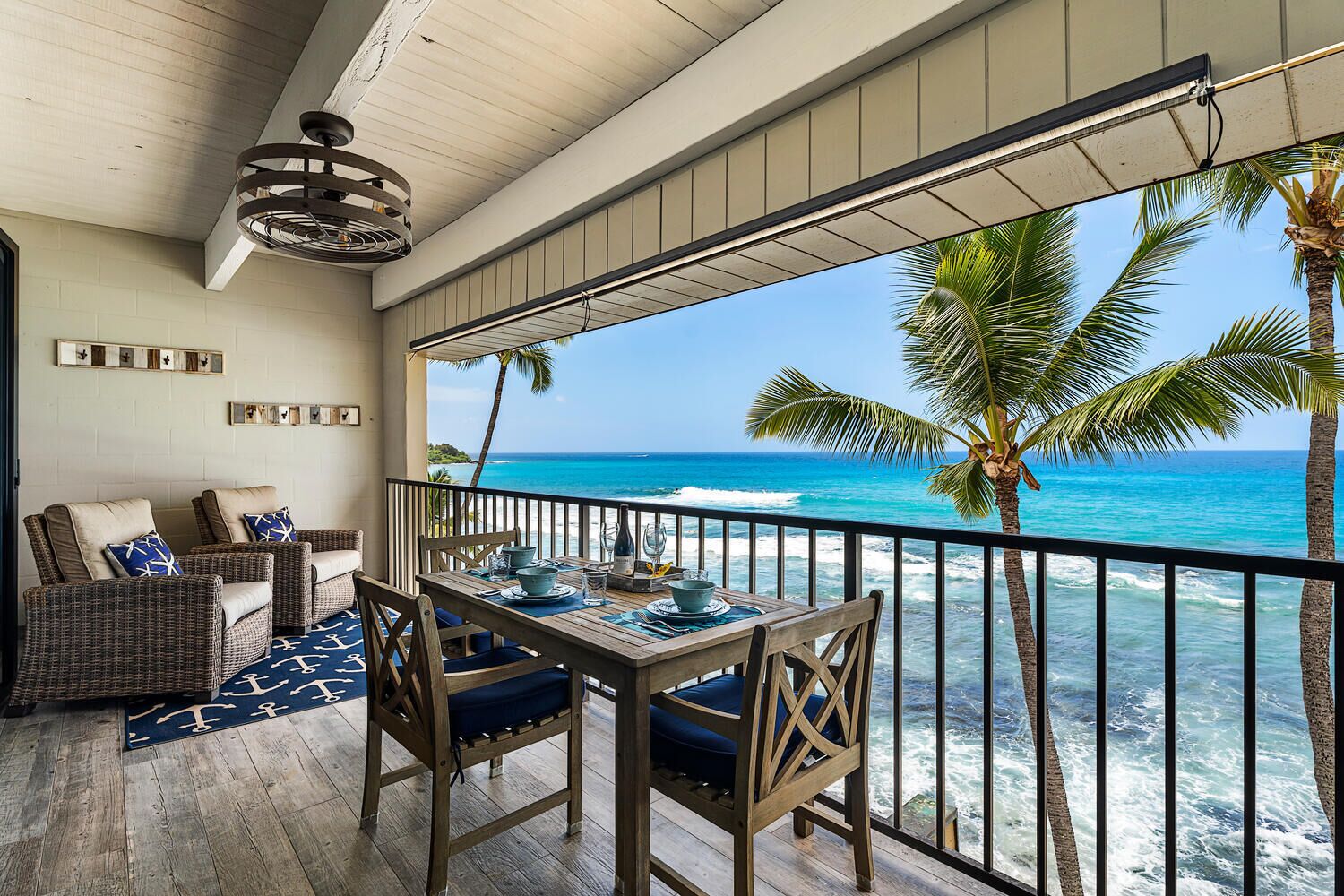 A balcony with a view of the ocean, furnished with wicker chairs and a table set for dining.