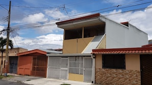 Un edificio residencial con techo plano, un pequeño balcón y entrada protegida por una reja.