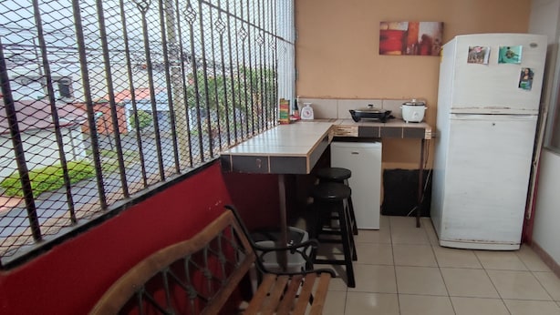 Una pequeña cocina con un refrigerador, estufa y lavamanos. Hay una ventana con una reja de metal y vistas al exterior.