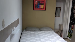 Una habitación pequeña y estrecha con una cama, un ventilador de techo, una lámpara y un cuadro en la pared.