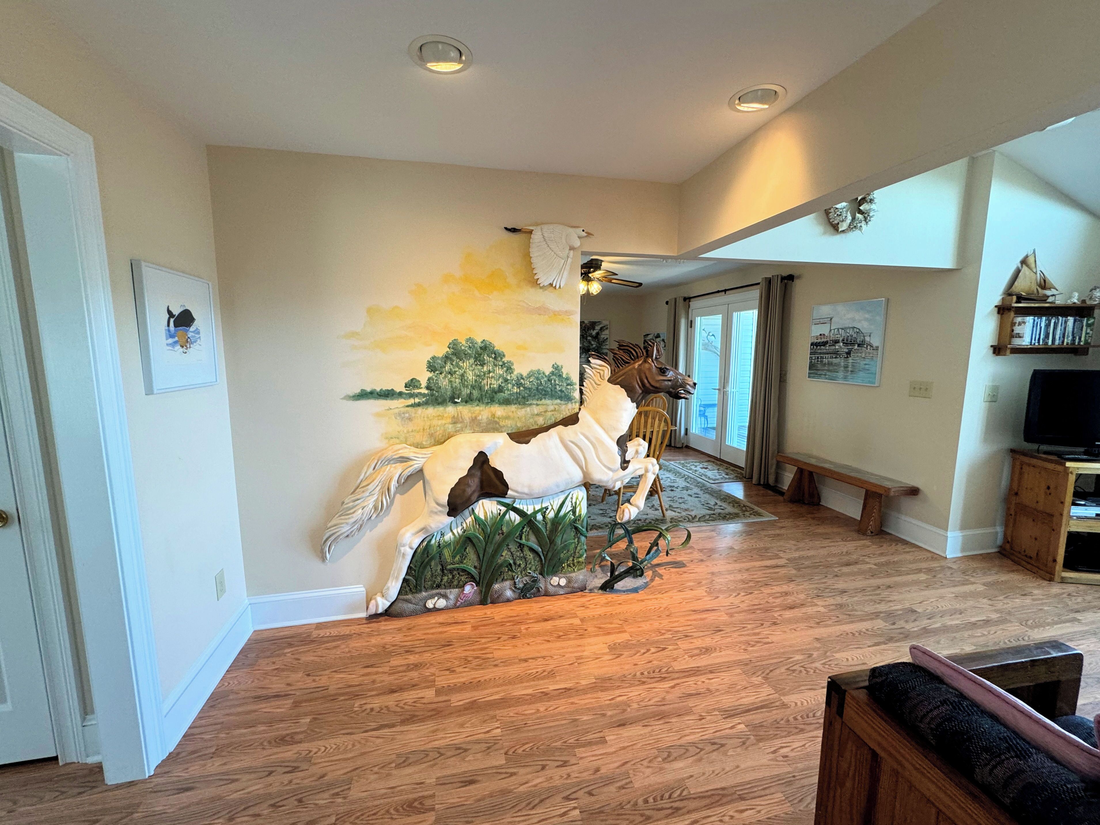 Amplio salón con un gran mural de un caballo, suelo de madera, un banco y un televisor sobre un mueble de madera.