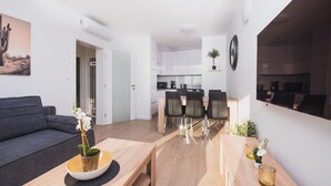 Een moderne woonkamer met een bank, een eettafel met stoelen, en een keuken op de achtergrond.