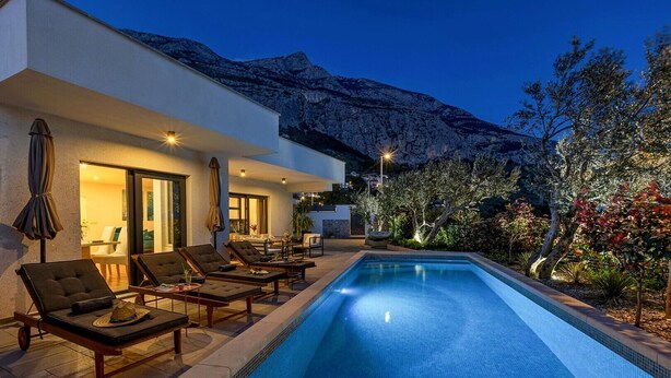 A swimming pool with lounge chairs, a dining area, and a mountain backdrop. - Villa Festina Lente in Makarska, heated pool (Makarska)
